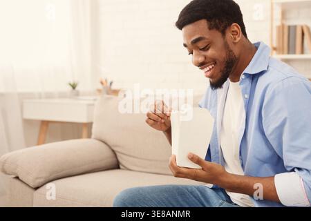 Junger afroamerikanischer Mann, der zu Hause asiatisches Essen isst Stockfoto