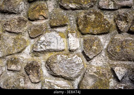 Nahaufnahme einer strukturierten Steinmauer aus unterschiedlich geformten Felsen, die Moos- und Flechtenwuchs in einer rustikalen Umgebung zeigt Stockfoto