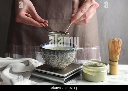 Frau, die Matcha-Pulver in eine Schüssel am weißen Tisch siebt, Nahaufnahme Stockfoto