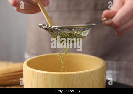 Frau, die Matcha-Pulver in eine Schüssel am Tisch siebt, Nahaufnahme Stockfoto