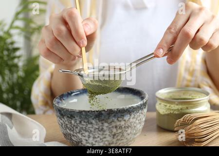 Frau, die Matcha-Pulver in eine Schüssel am Tisch siebt, Nahaufnahme Stockfoto