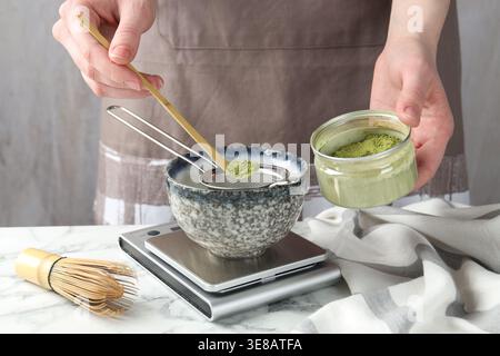 Frau, die Matcha-Pulver in eine Schüssel am weißen Tisch siebt, Nahaufnahme Stockfoto