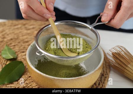 Frau, die Matcha-Pulver in eine Schüssel am weißen Tisch siebt, Nahaufnahme Stockfoto