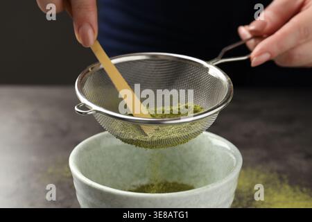 Frau, die Matcha-Pulver in eine Schüssel am grauen Tisch siebt, Nahaufnahme Stockfoto