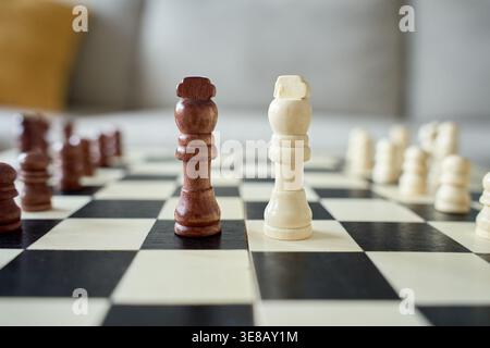 Schwarz-weiße hölzerne Schachköniginnen stehen auf Schachbrett mit verschwommenen Stücken im Hintergrund. Konzept von Strategie, Wettbewerb, Führung und Brettspiel. Stockfoto