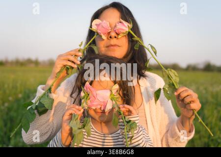 Mutter und Tochter spielen mit Rosen und Blumen auf Blumenwiese, lächeln und binden, Mutterschaft und Muttertag Stockfoto