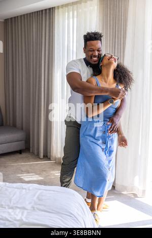 Verschiedene Paare stehen am großen Fenster im Schlafzimmer, umarmt neben weißem Bett und transparenten Vorhängen Stockfoto