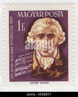 UNGARN - 20. September 1959: 1 Forint dunkelviolett, hellbraun und orange Briefmarke mit einem Porträt von Joseph Haydn, dem produktiven österreichischen Komponisten der Klassik. Die Illustration enthält seine Unterschrift und Notation aus „Rondo all'Ongarese“, einem Stück, das ungarischen Einfluss widerspiegelt. Haydn verbrachte den Großteil seiner Karriere als Hofmusiker für die wohlhabende Familie Esterházy auf ihren Ländereien in Ungarn. Diese Darstellung von 1959 erinnert an seinen historischen Einfluss auf die Sinfonie und das Streichquartett, zeitgleich mit seinem 150. Todestag Stockfoto