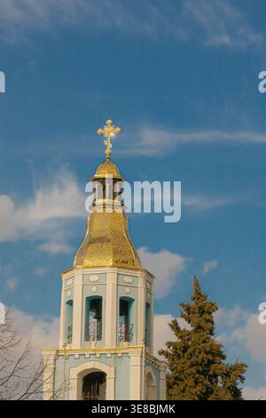 Orthodoxer Kirchturm mit goldener Kuppel und Kreuz, der sich gegen einen blauen Himmel mit weichen Wolken erhebt, in vertikaler Komposition, die religiöse A hervorhebt Stockfoto