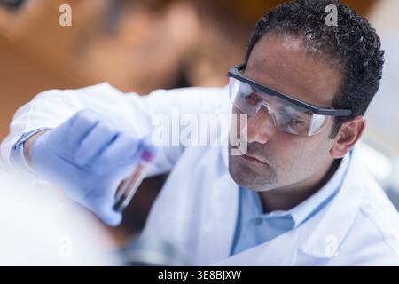 Ein junger Laborarzt mit Schutzbrille untersucht eine Blutprobe in einem medizinischen Testlabor Stockfoto