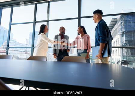 Glückliche Kolleginnen, die tagsüber in der Nähe des Teams im Konferenzraum im Büro die Hand schütteln Stockfoto