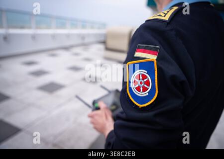 Warnemünde, Deutschland 13. April 2026 Übung vom Marinestützpunkt hohe Düne zur Erkennung einer Drohne im Bild: Soldat der Bundeswehr von der Deutschen Marine vom Marinestützpunkt hohe Düne bedient während einer Übung zur Drohnenerkennung und Drohnenabwehr eine Fernsteuerung im Hafenbereich von Warnemünde. Im Fokus steht ein Ärmelabzeichen mit maritimen Symbolen sowie die Deutschlandflagge auf der Uniform, während im Hintergrund die Steuerung eines unbemannten Fluggeräts genutzt wird. Die Einheit trainiert den Umgang mit Drohnentechnologie sowie deren Erkennung und Bewertung im sicherheitsrele Stockfoto