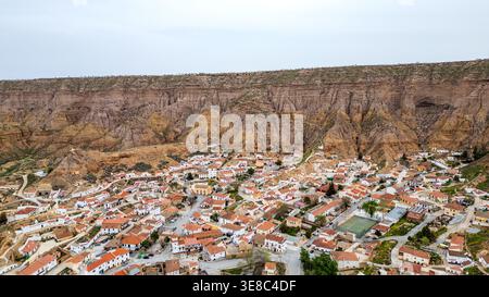 Ein Blick aus der Vogelperspektive fängt das malerische weiße Dorf Gorafe am Fuße einer imposanten Klippe im Granada Geopark ein. Typische Häuser mit roten Dächern Stockfoto