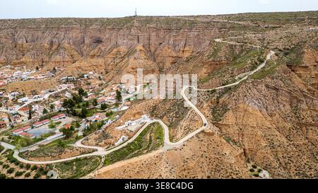 Dieses Panorama fängt das Dorf Gorafe am Fuße der hohen Klippen ein. Eine asphaltierte Straße schlängelt sich durch die Badlands des Granada Geoparks, SH Stockfoto