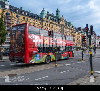 Stockholm, Schweden - 11. Oktober 2025: Roter Doppeldecker Hop-on-Hop-off-Sightseeing-Bus, der auf einer Stadtstraße mit historischem gelbem Gebäude und Ornat fährt Stockfoto