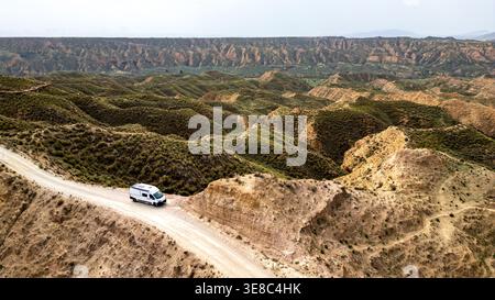 Ein weißer Wohnmobil fährt eine Feldstraße entlang eines Berges im Granada Geopark. Diese Luftaufnahme fängt die Weite der Badlands, erodierten Hügel und ein Stockfoto