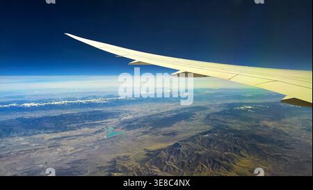Flugzeugflügel über Wüstenberglandschaft. Aus der Vogelperspektive eines Passagierflugzeugs zeigt einen langen Flügel über zerklüfteten Bergen und Wüstentälern Stockfoto