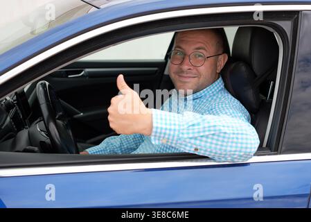 Glücklicher Mann im Auto zeigt Daumen hoch Fahrererfolgkonzept Stockfoto