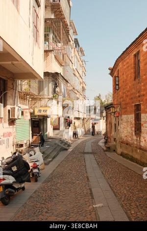 Eine enge Kopfsteinpflasterallee schlängelt sich zwischen verwitterten Backsteinhäusern und modernen Wohnblocks in einem alten chinesischen Viertel mit geparkten Motorrollern Stockfoto