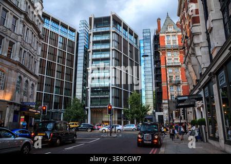 Schwarze Taxis und Verkehr füllen eine geschäftige Straße, in der moderne Glasbürogebäude im Kontrast zur viktorianischen Backsteinarchitektur in London, England, stehen Stockfoto