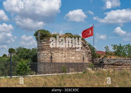 Theodosianische Mauern oder historische Mauern der Ruinen von Konstantinopel, Istanbul, Türkei. Die türkische Flagge fliegt über dem alten, von Vegetation bewachsenen Steinbau unter hellblauem Himmel mit weißen Wolken Stockfoto