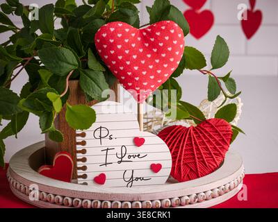 Einrichtung in Rot und weiß am 14. Februar zum Valentinstag. Rustikales Tablett mit romantischem Schild und PS I LOVE YOU Text, Garnherzen, Grün und weiches Herz Stockfoto