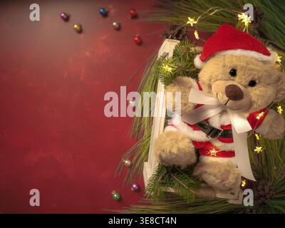 Hintergrund für personalisierte Weihnachtskarte. Roter Texturhintergrund mit Teddybär in Santa Claus Kleidung, in einer Kiste und Fichtenzweigen Stockfoto