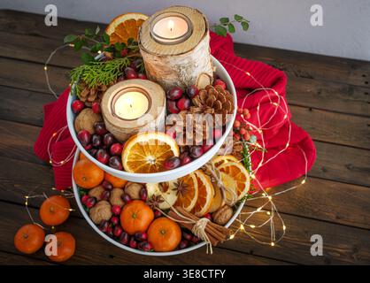 Herbst festliche Weihnachtsdekoration weißes Tablett mit Birkenrindenkerzen, Tannenzapfen, Preiselbeeren, Walnüssen, Orangen, roter Pullover und Feenlichter Stockfoto