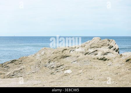 Geschichtete Küstengesteinsformation an einer japanischen Küste vor einem ruhigen, hellblauen Meer und Himmel, geologische Schichten zeigen Zeit und natürliche Kraft. Eine minimalistische und besinnliche Meereslandschaft, ideal für Natur- und Reiseinhalte. Stockfoto