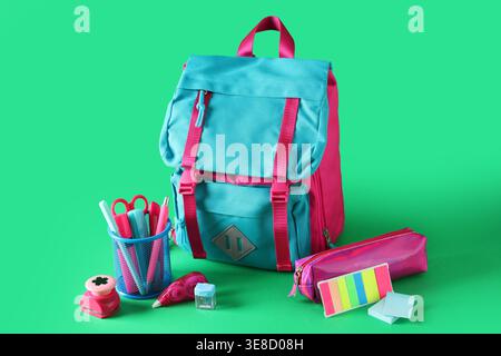 Stylischer Schulrucksack und verschiedene Schreibwaren auf grünem Hintergrund Stockfoto