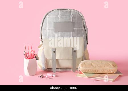 Stilvoller Schulrucksack und verschiedene Schreibwaren auf rosa Hintergrund Stockfoto