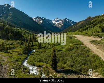 Aus der Vogelperspektive auf einen Gletscherbach, der durch ein üppiges Bergtal in der Nähe von Animas Forks, Colorado fließt. Schroffe Berggipfel unter klarem Sommerhimmel. Stockfoto