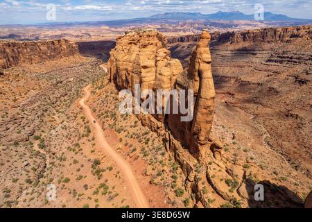 Aus der Vogelperspektive eines Fahrzeugs auf der gewundenen Long Canyon Road, Utah. Hochwinkelaufnahme einer massiven Sandsteinflosse und einer zerklüfteten Wüstenlandschaft unter einem blauen Himmel. Stockfoto