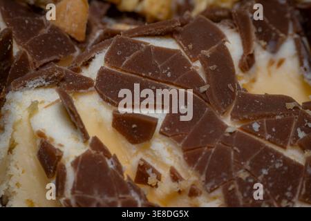 Detaillierte Nahaufnahme von fragmentierten Milchschokoladenstücken, eingebettet in weiches Vanilleeis auf einem Dessert, mit Textur und Kakaodetails Stockfoto