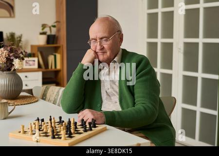 Senior Kaukasier, der zu Hause Schach spielt, Strategie und kognitive Herausforderung durchdenkt. Nützlich für Ruhestand Lebensstil, Gedächtnis Gesundheit, Konzentration, Solo Freizeit Marketing Stockfoto