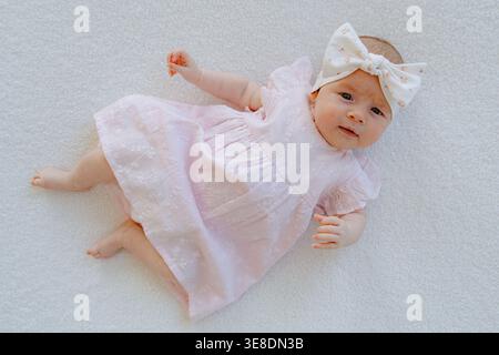 Mädchen in rosa Kleid auf weißem Hintergrund, von oben gesehen. Minimale Zusammensetzung mit Kopierraum bereinigen. Ideal für Eltern und Babyprodukte Stockfoto