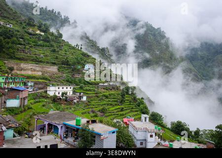 Dieses Bild zeigt eine ruhige Dorflandschaft in der Nähe des Madhyamaheshwar Tempels in Uttarakhand, Indien. Die Szene ist umgeben von üppigen grünen Bergen und Stockfoto