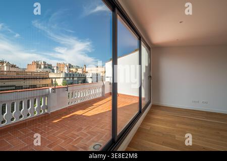 Modernes, leeres Apartment mit großen Glastüren, die zu einem Balkon führen. Helles Tageslicht beleuchtet den Holzboden und die weißen Wände. Stockfoto