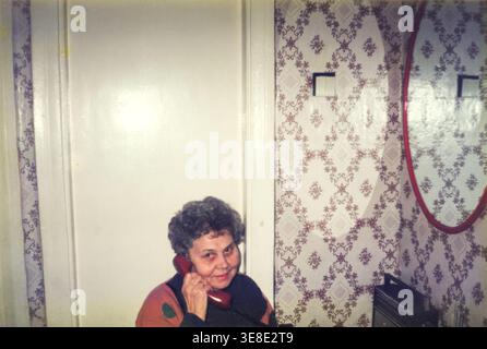 Eine ältere Frau, die auf dem Festnetztelefon in einem alten Flur spricht Stockfoto