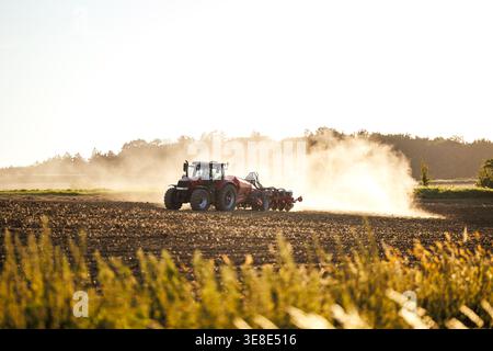 Traktor mit Sämaschine zur Aussaat von Erntegut auf staubigem Feld. Landwirtschaftsmaschinen zur Bodenbearbeitung und zum Anpflanzen von Saatgut auf dem Land. Landwirtschaftliche Tätigkeit Stockfoto