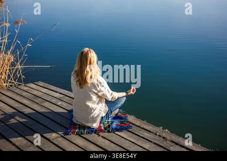 Meditation in Lotusstellung auf Holzsteg. Frau, die Yoga am Dock am See praktiziert, findet inneren Frieden in ruhiger Natur Stockfoto
