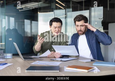 Zwei verschiedene Geschäftsleute diskutieren in einem modernen Büro über frustrierende Dokumente und zeigen Stress und Enttäuschung über unerwartete geschäftliche Probleme und Fehler Stockfoto