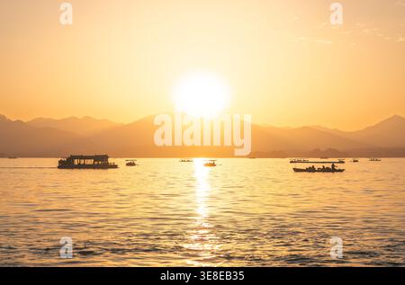 Goldener Sonnenuntergang über dem Westsee mit traditionellen Booten für Passagiere in Hangzhou, China Stockfoto
