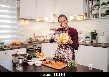 Frau, die frisches Gemüse in Schüssel hält, gesunde Mahlzeit in der modernen Küche zubereiten Stockfoto