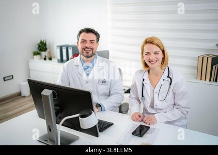 Zwei medizinische Fachkräfte sitzen an einem Schreibtisch und lächeln in einer Klinik Stockfoto