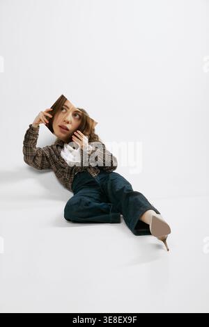 Junge Frau, die auf dem Boden liegt und ein bedrucktes Gesicht hält, kreatives Modestudio-Porträt Stockfoto