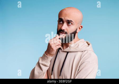 Arabischer Mann, der Entscheidungen trifft, das Kinn nachdenklich berührt und wegblickt. Junge kahlköpfige bärtige Person mit nachdenklichem Gesichtsausdruck, die über Problemlösung nachdenkt Stockfoto