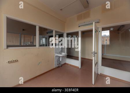 Innenansicht eines Patientenzimmers in einer stillgelegten russischen Kinderklinik. Verfügt über ein altes Keramikwaschbecken, Glastrennwände und abgenutzte Wände von der p Stockfoto