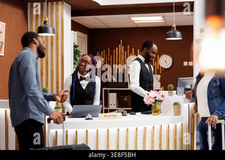 Angenehmes Gespräch zwischen Rezeptionist und Gast im Hotel. Freundliche, lächelnde junge afroamerikanische Empfangsangestellte begrüßte die Gäste an der Rezeption und half beim Check-in Stockfoto