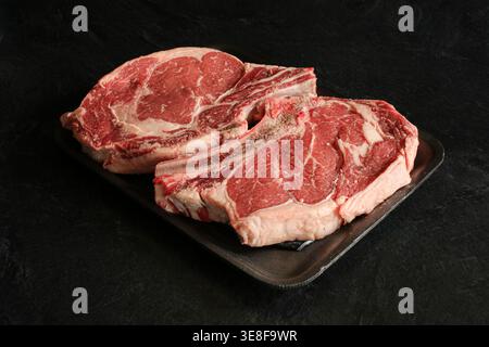 Frische Steaks mit Rippenaugen auf schwarzem Hintergrund. Stockfoto